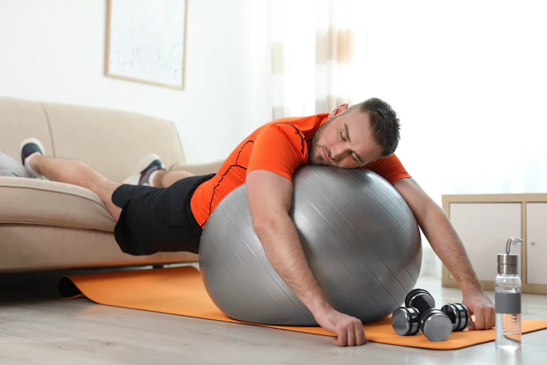 Un jeune homme en tenue de sport est effondré sur un ballon d'exercice et son canapé