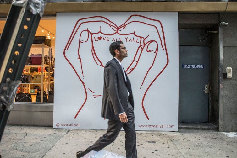 Man walks by billboard with text reading 'love all y'all.'