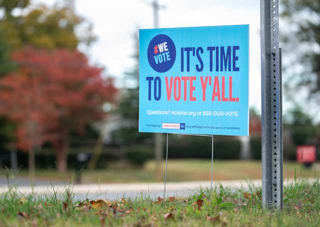 A blue lawn sign reads 'It's Time to Vote Y'all.'