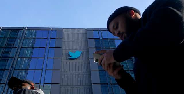 A person seen walking in front of the Twitter building holding a phone.