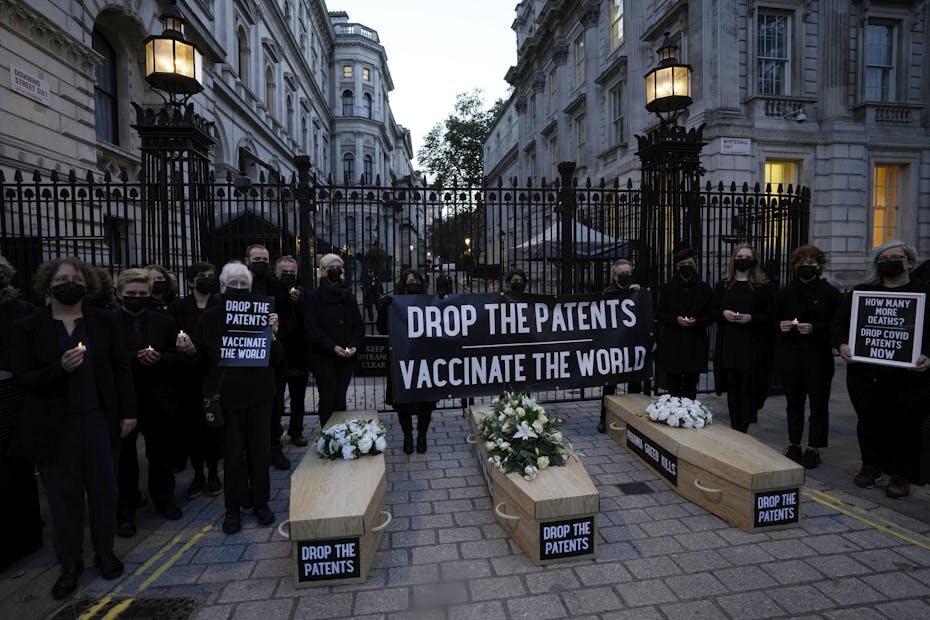 People stand next to fake coffins with signs that say 'drop the patents.'