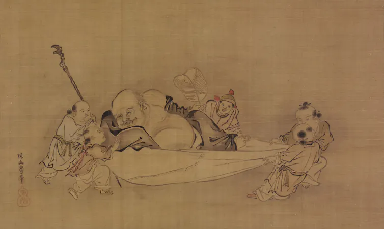 A monk lying on a bed while children tug at the sheet and play with him.