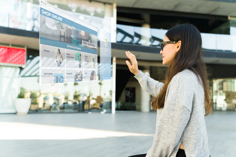 A woman wearing virtual realty glasses scrolls through a virtual online shopping page that is displayed in mid-air