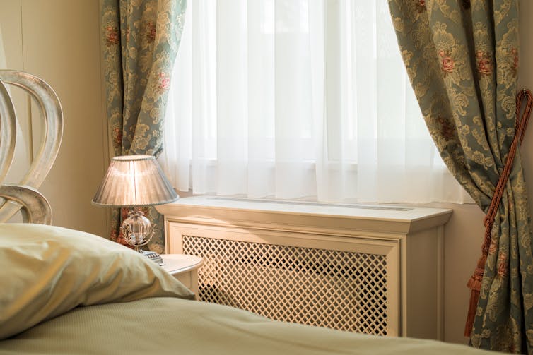 A radiator covered in a wooden casing next to a bed.