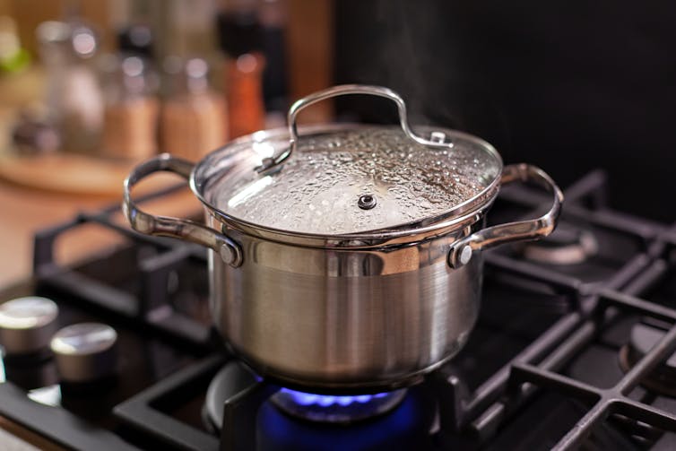 A pan on an gas stove with steam condensing on the lid.