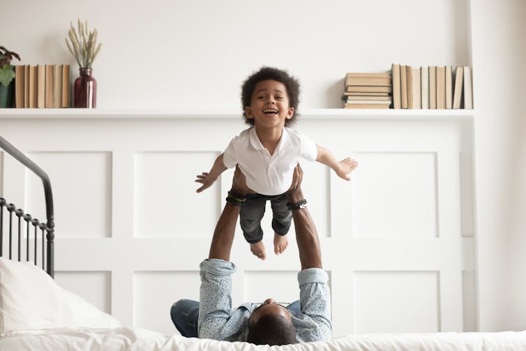 Father lying on a bed lifting his young son up