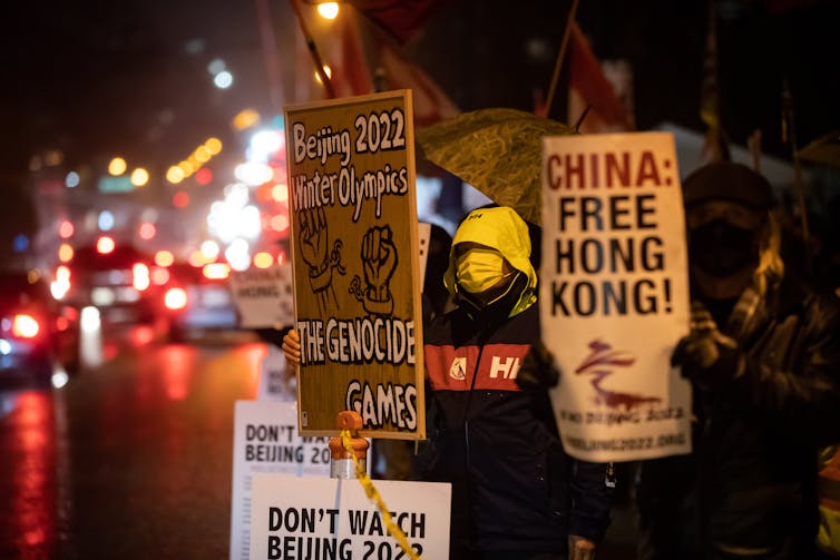 Protesters hold signs, including one reading Free Hong Kong, on a city street at night.