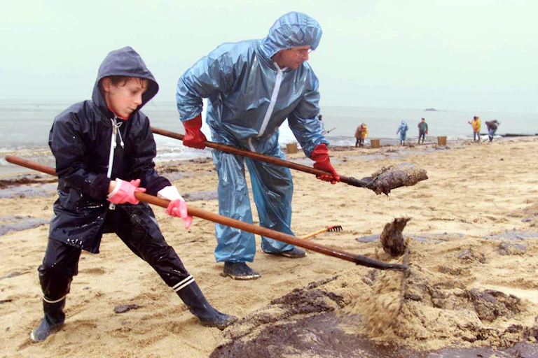 Une enfant et son père nettoient une plage souillée après le naufrage d'un bateau pétrolier en 1999