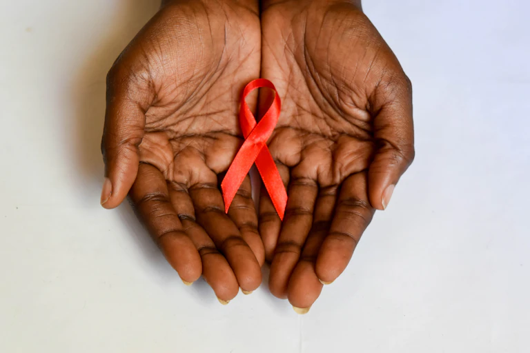African dark brown skin cupped hands holding red ribbon