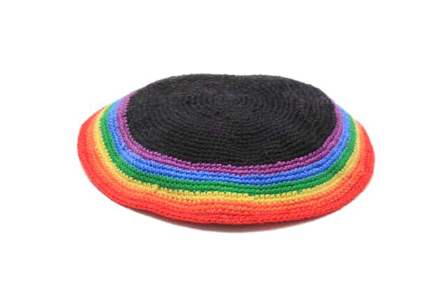 A Jewish head covering for men, stitched with rainbow colors, against a white background.