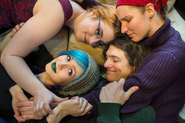Four young adults lying together and embracing one another.