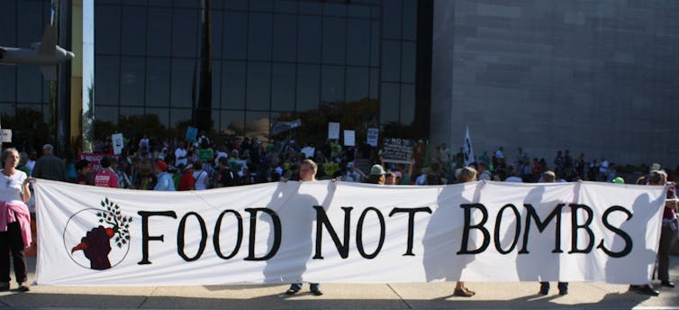 People seen standing with a banner that says 'Food Not Bombs.'