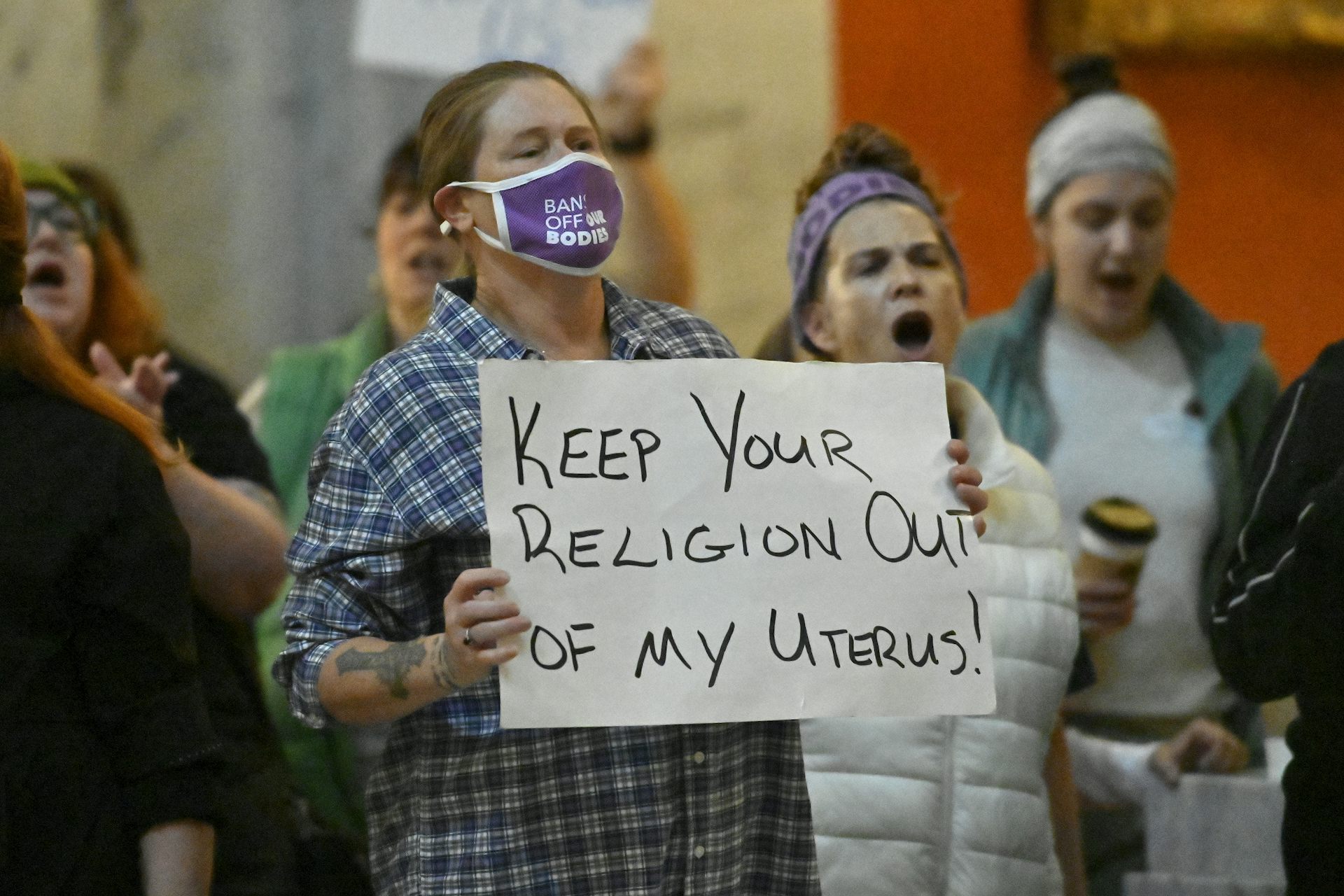 A woman wearing a mask that says bans off our bodies carries a sign that reads Keep Your Religion Out of my Uterus.