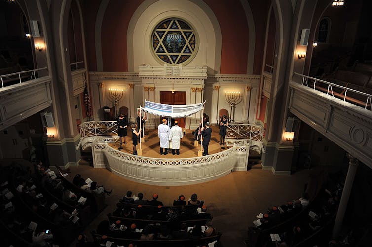 A dark synagogue with two men getting married at the front of the room.