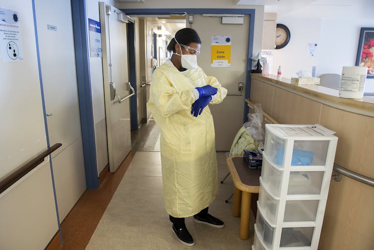 A nurse in puts on a protective gown, gloves, and mask in a care home