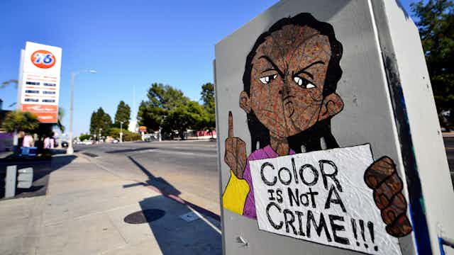 A drawing of Riley Freeman – a character from "The Boondocks" cartoon TV show – has been drawn on a utility box near a gas station. He is holding a sign that says "Color is not a crime!!!"
