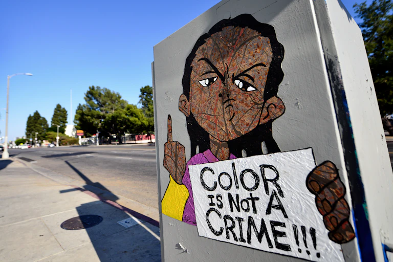 A drawing of Riley Freeman – a character from "The Boondocks" cartoon TV show – has been drawn on a utility box near a gas station. He is holding a sign that says "Color is not a crime!!!"