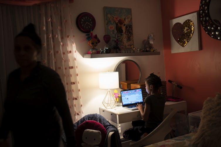 A young child sits at a desk in front of a computer