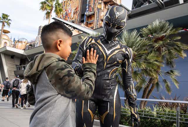 Boy high-fives a man dressed up in a Black Panther costume.