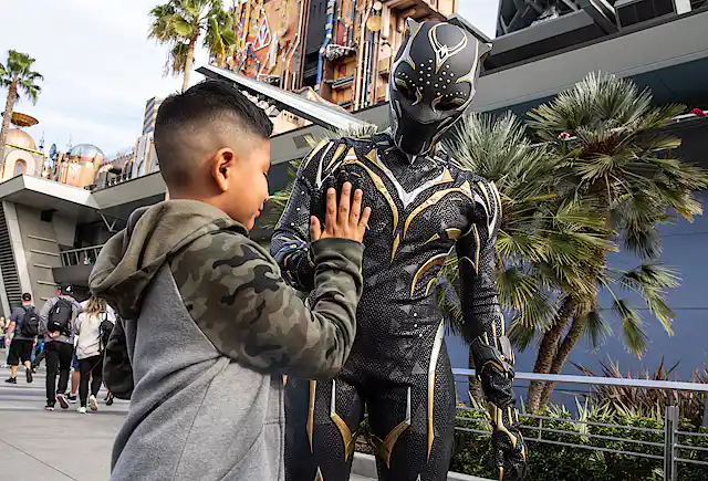 Boy high-fives a man dressed up in a Black Panther costume.