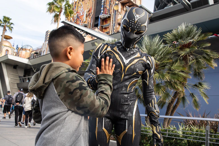 Boy high-fives a man dressed up in a Black Panther costume.