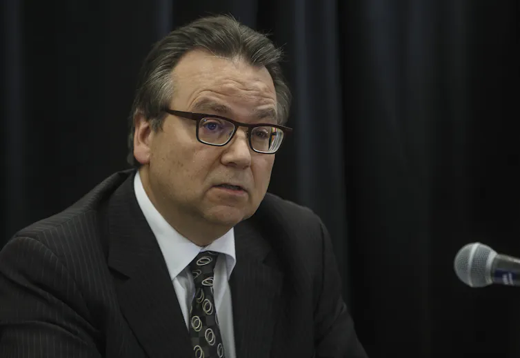 A close-up shot of a man in a suit and glasses speaking into a microphone