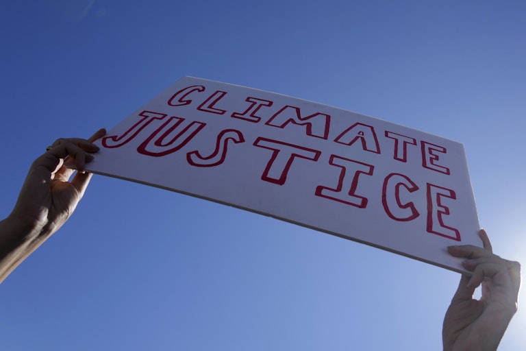 Hands hold a sign reading "climate justice