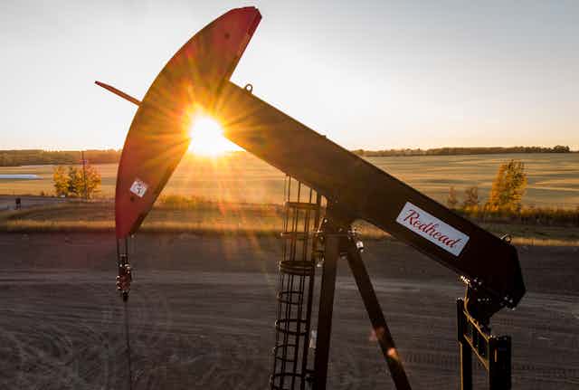 A pumpjack sitting in a field in front of the setting sun
