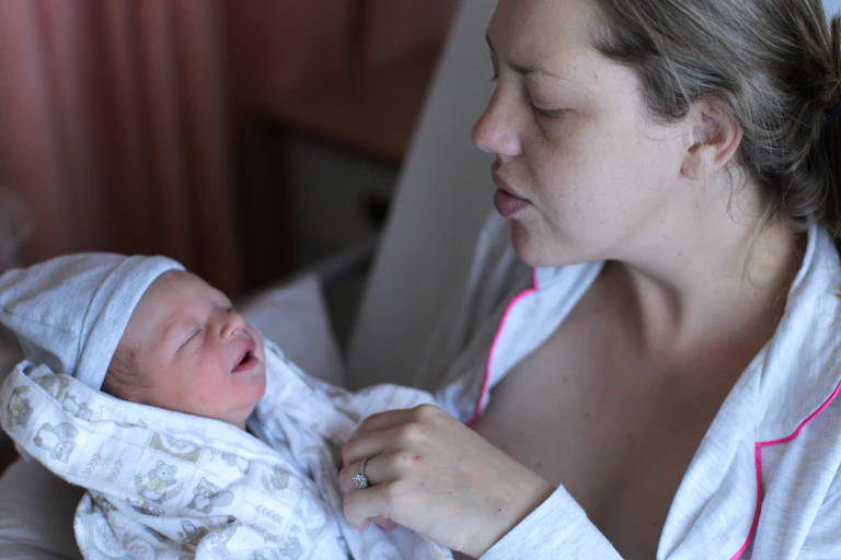 A young woman holds and soothes her newborn baby.