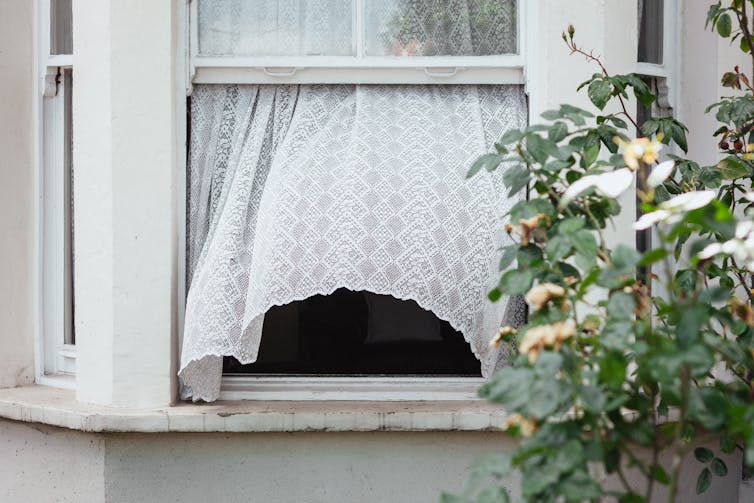 Wind blows curtain through open window of an old terrace house