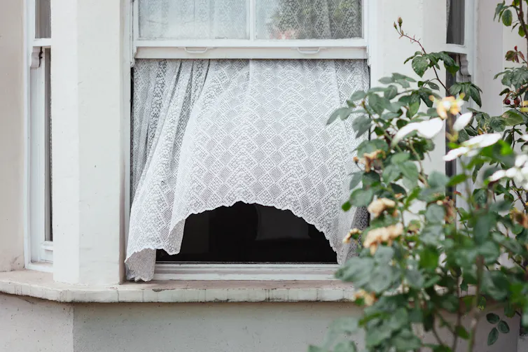 Wind blows curtain through open window of an old terrace house