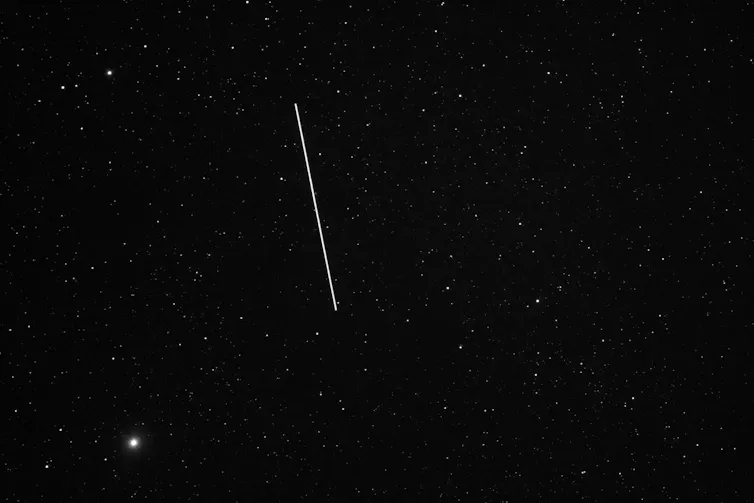 A starry sky with a black background and a white line trailing across it