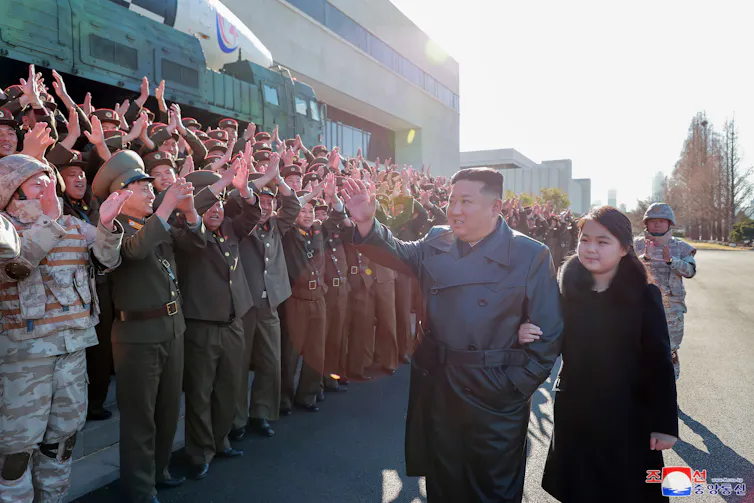 Kim Jong-un waves to crowds with his daighter to his left, arm in arm.