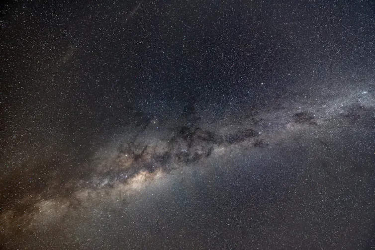 The night sky in charcoal and dark yellow tones, with the Milky Way streaking across on a diagonal