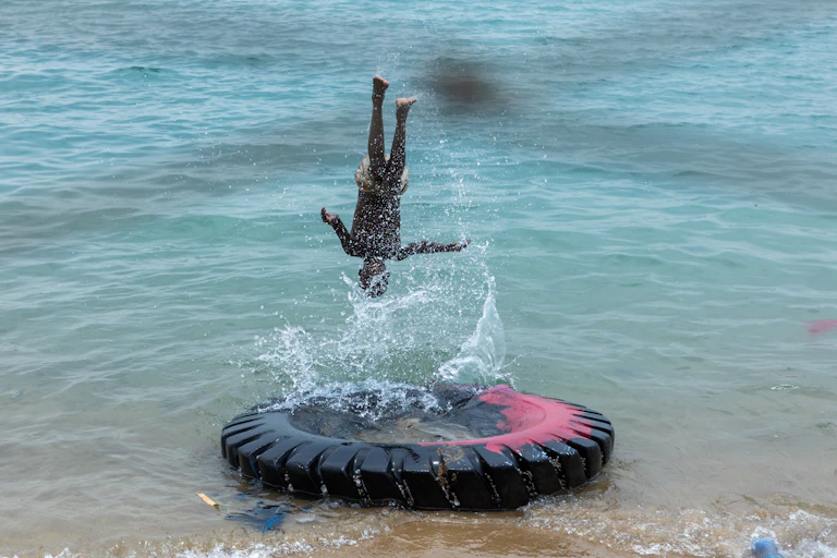 A boy turns a somersault above a large tyre partially submerged in blue-green seawater