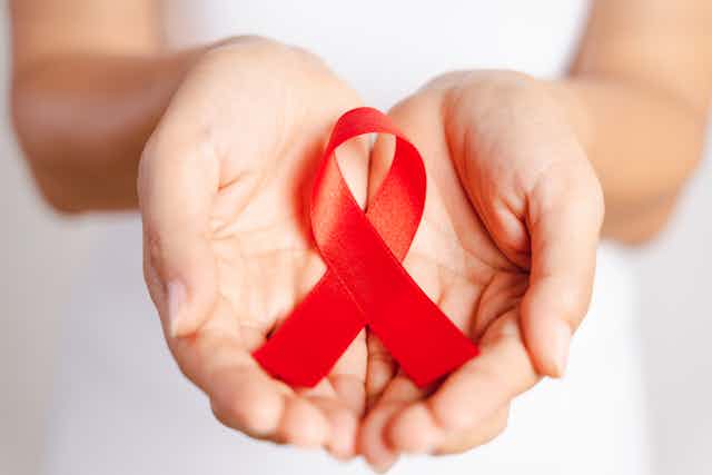 Woman hand holding red ribbon HIV, world AIDS day awareness ribbon.