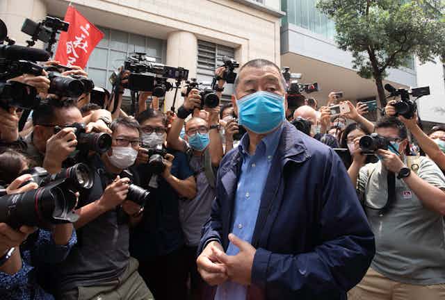 A ma wearing a blue mask is surrounded by photographers.