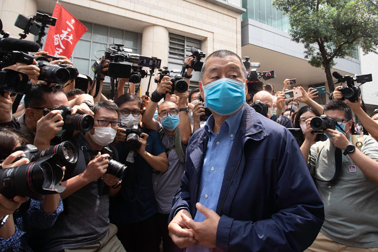A ma wearing a blue mask is surrounded by photographers.