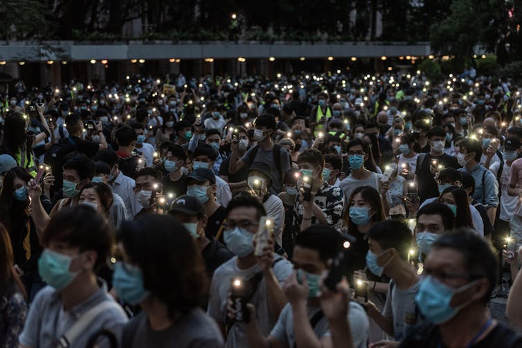 Hundreds of people sit in a square with lights and candles.