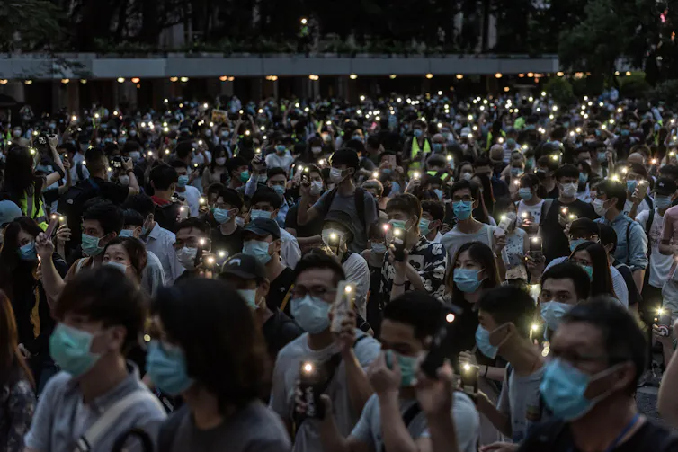 Hundreds of people sit in a square with lights and candles.