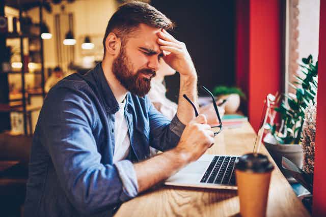 A man working on his laptop looks frustrated.