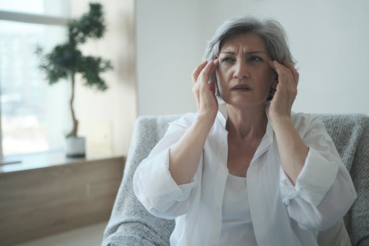 A woman looks troubled, and has her fingers to her temples.