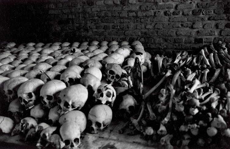 A black and white photo shows rows of stacked human skulls and bones.