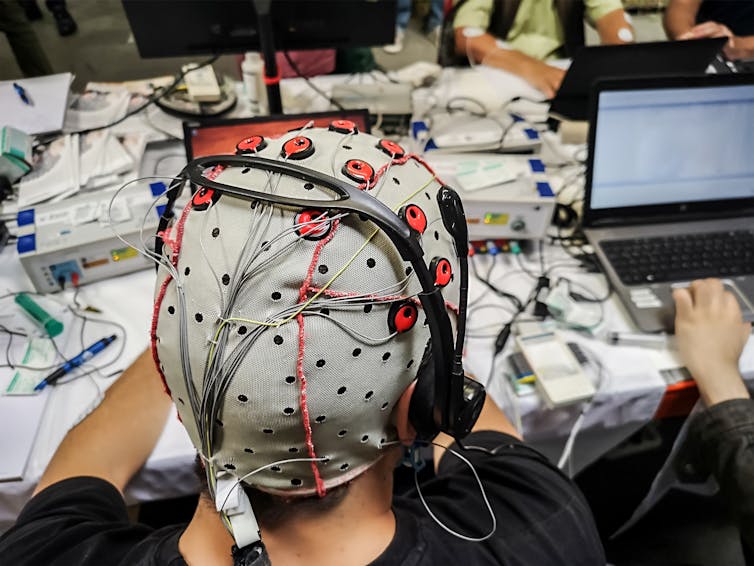 Person using a brain-computer interface, wearing an EEG cap connected to a laptop