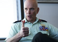 A bald man in a military shirt gives the thumb's up.