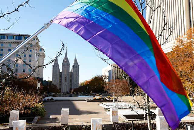 A rainbow flag flies on a street, with a cathedral-like building in the distance.