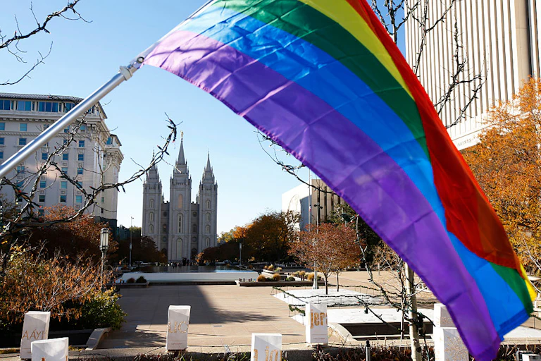 A rainbow flag flies on a street, with a cathedral-like building in the distance.