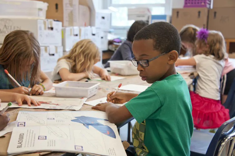 Children in a classroom with windows closed write in workbooks.