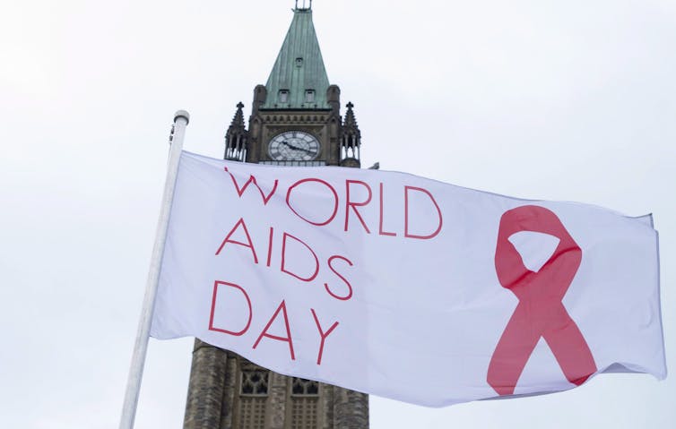 A white flag with the words World Aids day and a red ribbon flies in front of the peace tower.