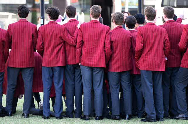 Private school boys stand in a line with their backs to the camera.